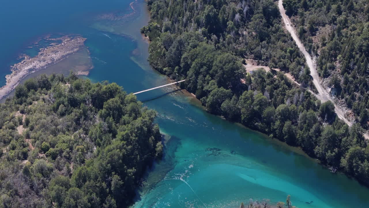 fotografía aérea de un puente colgante en medio de un bosque prístino y aguas claras en la patagonia, argentina.