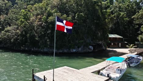 Aerial-orbit-shot-of-waving-flag-of-Dominican-Republic-on-wooden-jetty-of-Los-Haitises-National-Park