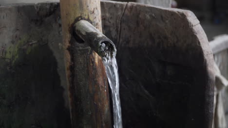 Agua-Limpia-Y-Clara-Que-Fluye-Del-Pico-De-Una-Fuente-De-Bambú-Y-Madera