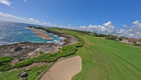 Vuelo-Fpv-Sobre-Una-Hermosa-Cancha-De-Golf-Verde-Y-Una-Costa-Rocosa-Con-Un-Paisaje-Marino-Caribeño-Azul-En-Verano