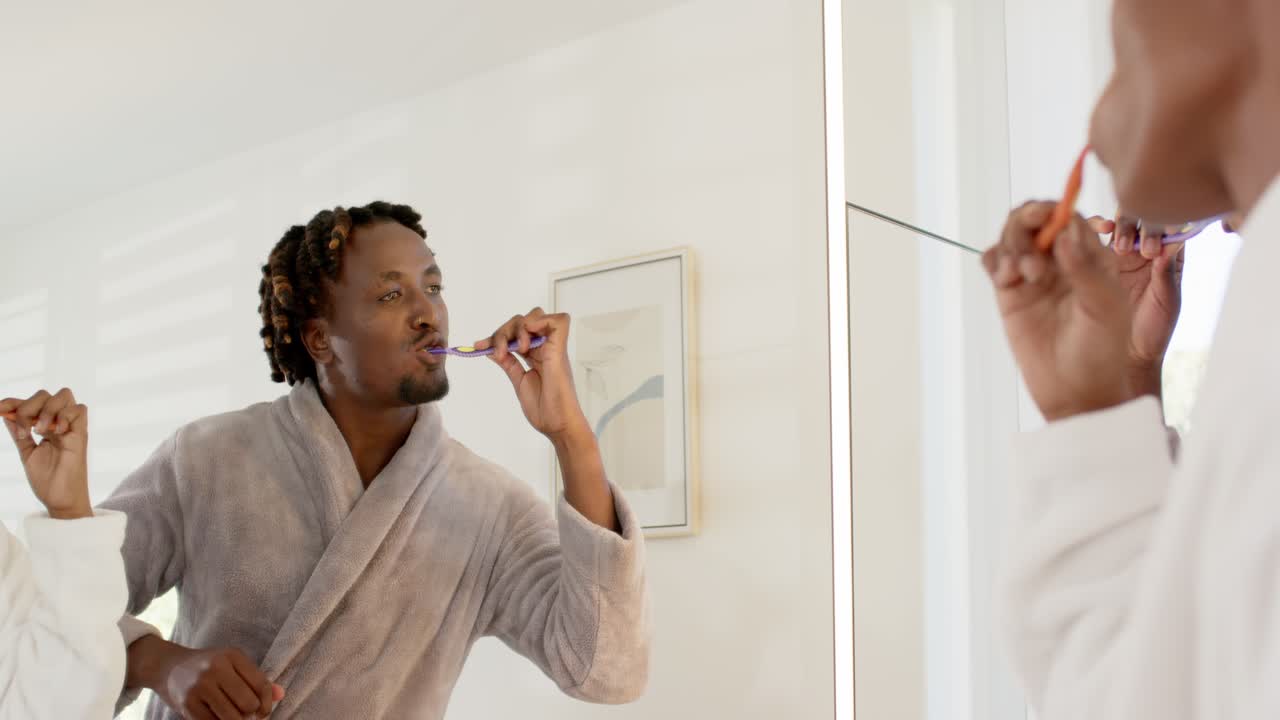 Coppia afroamericana che si lava i denti allo specchio, routine mattutina che inizia con spazzolini da denti colorati.