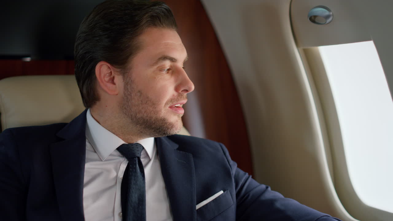 Manager termina telefonata su jet primo piano. Uomo fiducioso guarda finestrino aereo.
