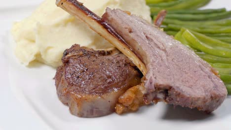 tiro deslizante de chuletas de cordero en un plato blanco con puré de patata y judías verdes