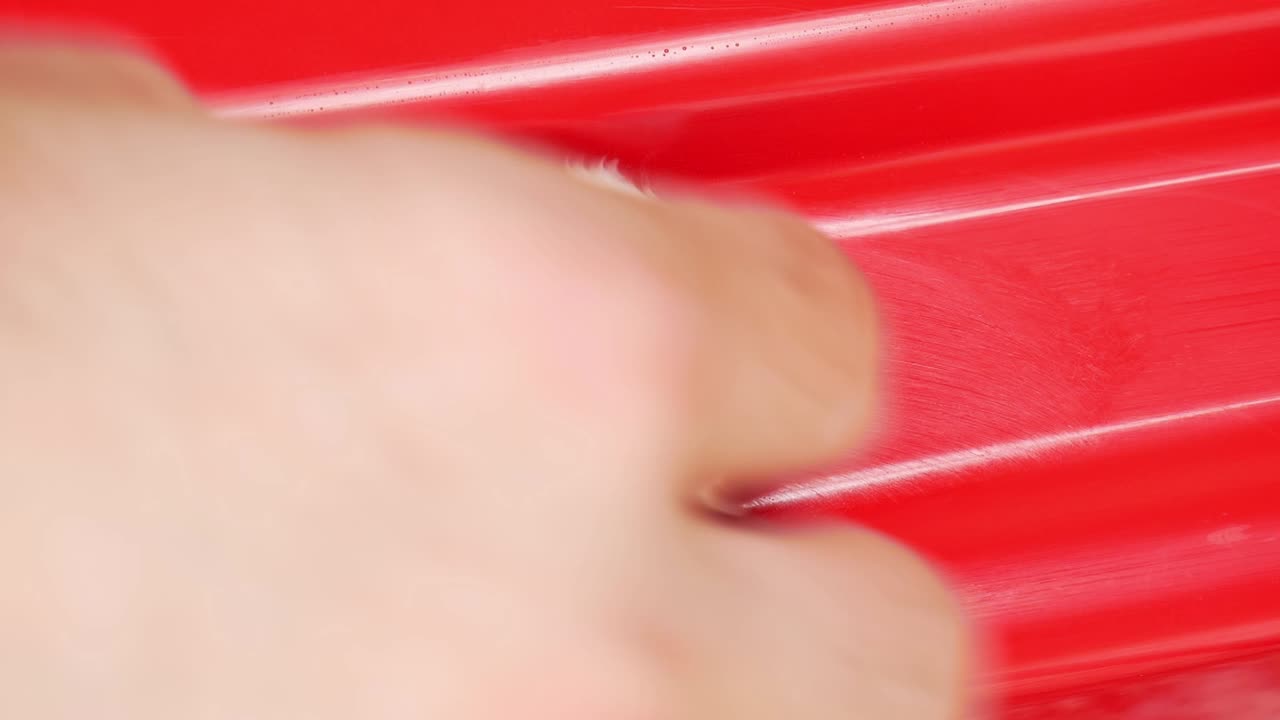 Extreme close up hand polishing a scratch from red car door shut with white microfibre pad