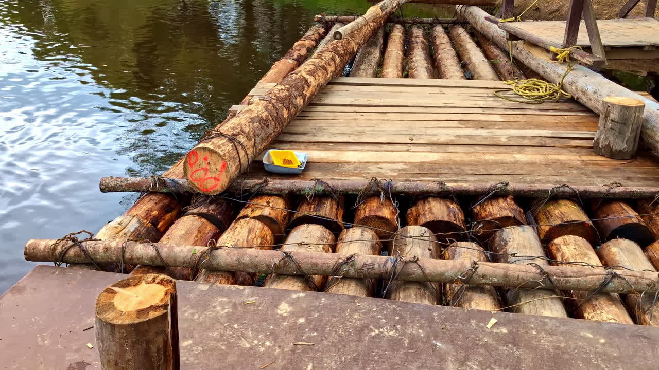 Floating wooden raft built from logs and planks tied with wire on riverbank