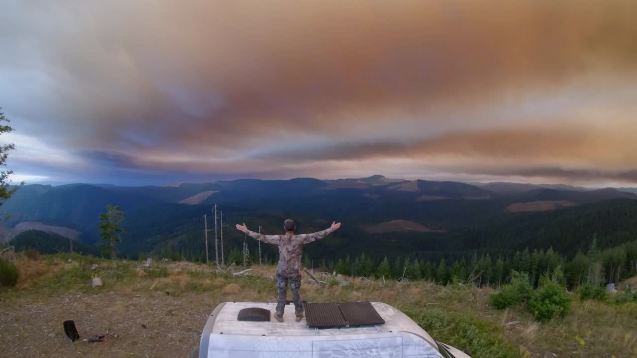 hombre en la parte superior de la furgoneta, con las manos en alto durante la puesta de sol de incendios forestales, velocidad de fotogramas 59