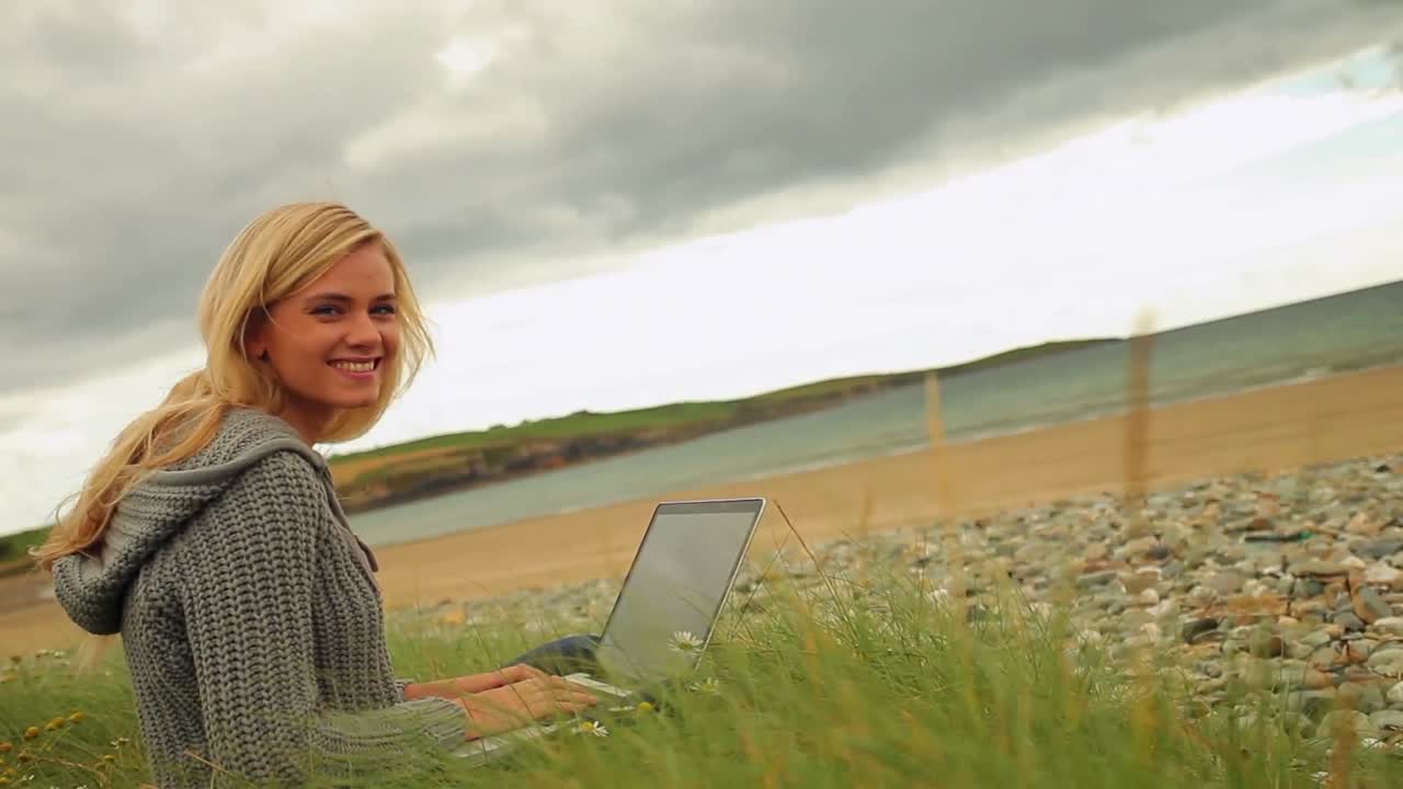 Pretty blonde using laptop by the beach
