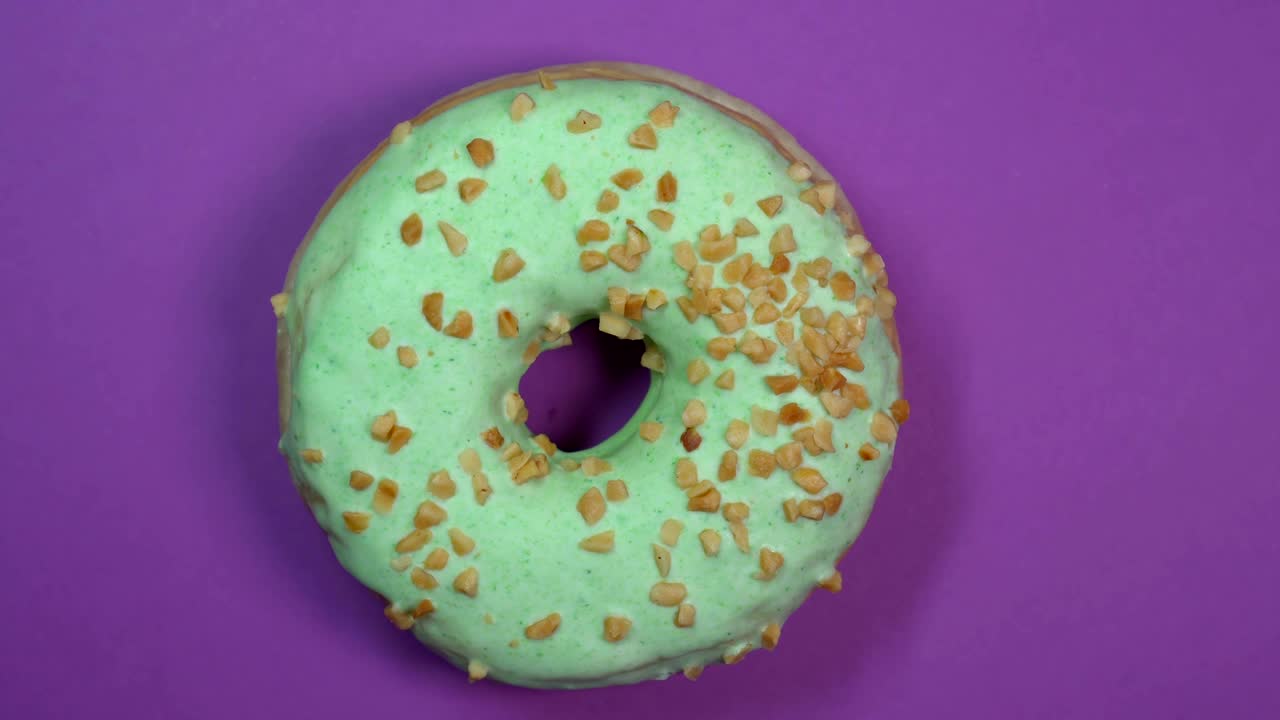 donut vidriado verde brillante con nueces en primer plano, macro disparado, girando sobre un fondo púrpura.