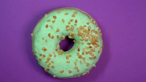 donut vidriado verde brillante con nueces en primer plano, macro disparado, girando sobre un fondo púrpura.