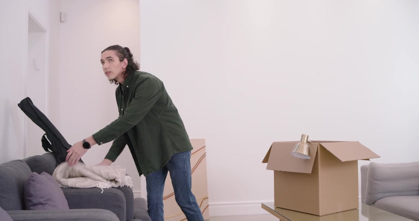 Uomo afroamericano che apre una scatola, disimballa un cuscino, sistema un plaid e posiziona una lampada, preparando la casa.