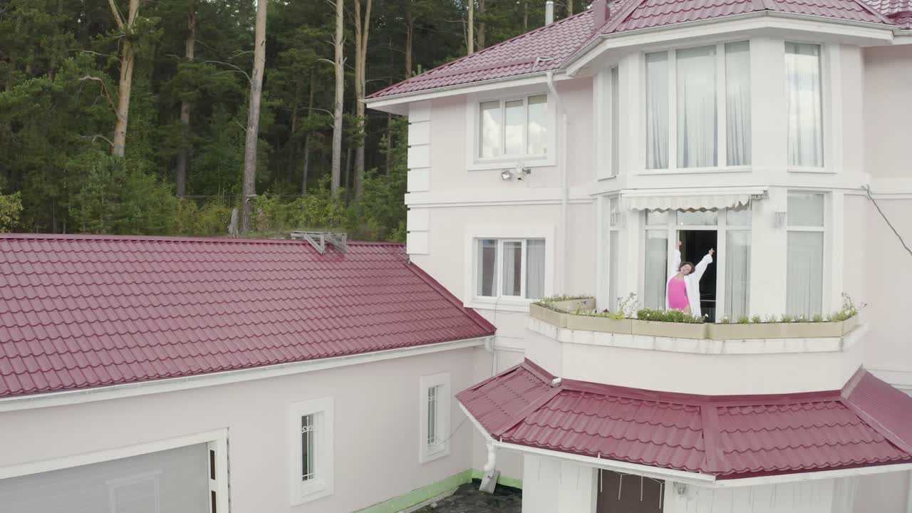 mujer en el balcón de una casa rosa