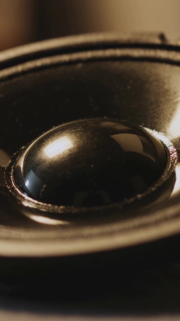 Vertical video: Showing speaker dome driven by sound, vibrating then settling in room with sheen