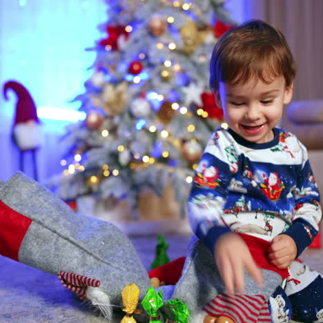 happy caucasian baby getting the candies from the christmas stockings. adorable child celebrating and rejoicing holidays.