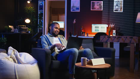 vertical video adult guy typing on laptop laying on couch in stylish apartment