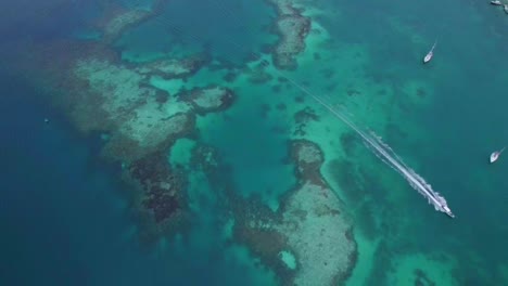 Boat-passing-through-the-turquoise-sea-water-over-a-tropical-coral-reef