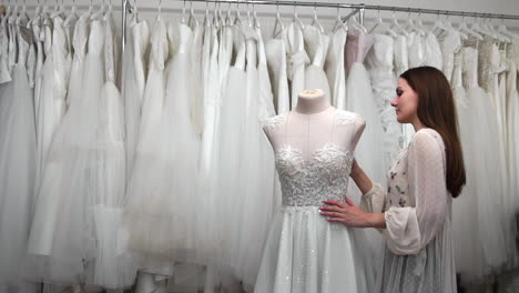 hermosa niña buscando vestido de novia en la cabina en comparación con otros vestidos. preparando para la boda. comprando un vestido de novia. la costurera inspecciona el vestido de novia hecho a medida terminado.