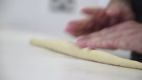 primer plano de un panadero extendiendo una cuerda de masa para hacer pan trenzado