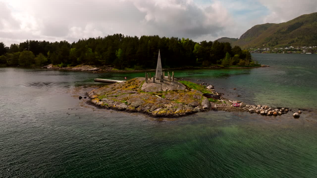Drone approach orbit to Solspeilet stone circle on water’s edge in Jorpeland, surrounded by green hills