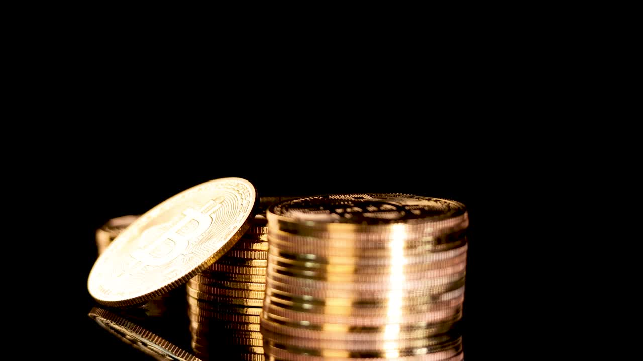 Gold Bitcoin coin spins on stacked coins, black background, dramatic studio lighting, smooth camera movement