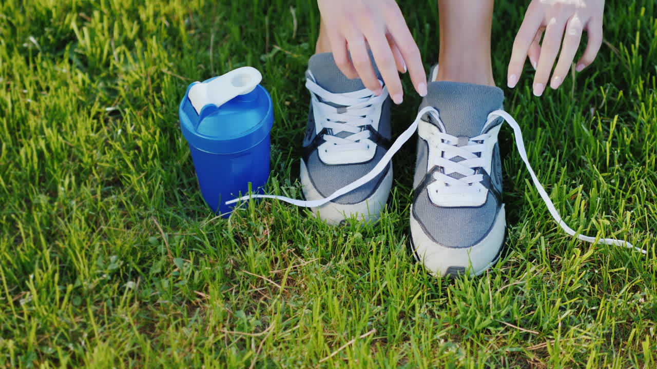 ate los cordones de los zapatos deportivos piernas femeninas en un césped verde cerca de una botella de agua lista para una actividad