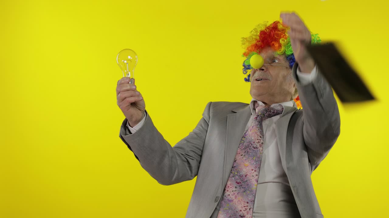 Anziano imprenditore clown mostra una lampadina. Ha avuto una grande idea.