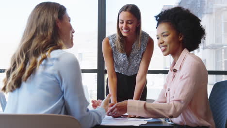 Female-Multi-Cultural-Business-Team-Meet-Around-Boardroom-Table-With-Laptops-Discussing-Documents