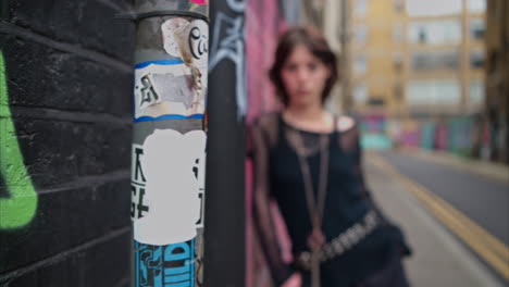 retrato de moda al aire libre de una mujer joven de estilo alternativo apoyándose en una pared cubierta de graffiti en la calle de la ciudad de londres, reino unido, en tiempo real.