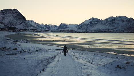 a person handling a tripod is going on the beach in lofoten islands in winter