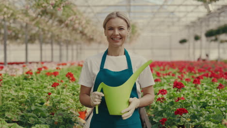 smiling woman gardener holding watering can in a greenhouse