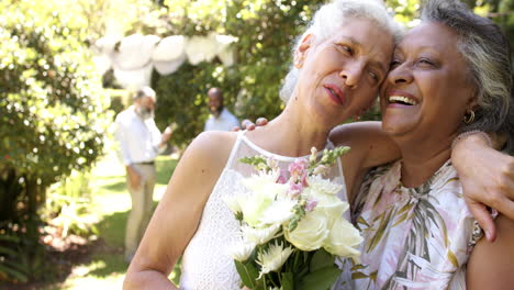 smiling senior bride and bridesmaid hugging and holding bouquet of flowers at outdoor wedding