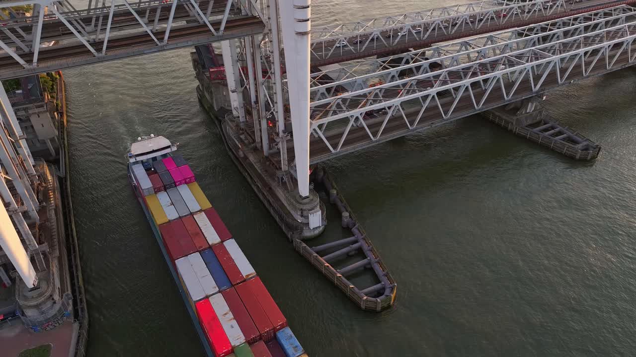Aerial view of a cargo ship passing under a bridge with colorful shipping containers