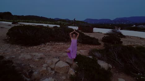 woman meditating in yoga position on a cliff overlooking the sea at sunset in ibiza. nice aerial view flight fly reverse drone