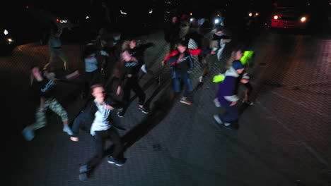 guys dancing hip hop outdoors at night in the flashlight. cars with headlights on standing at backdrop. view from above.