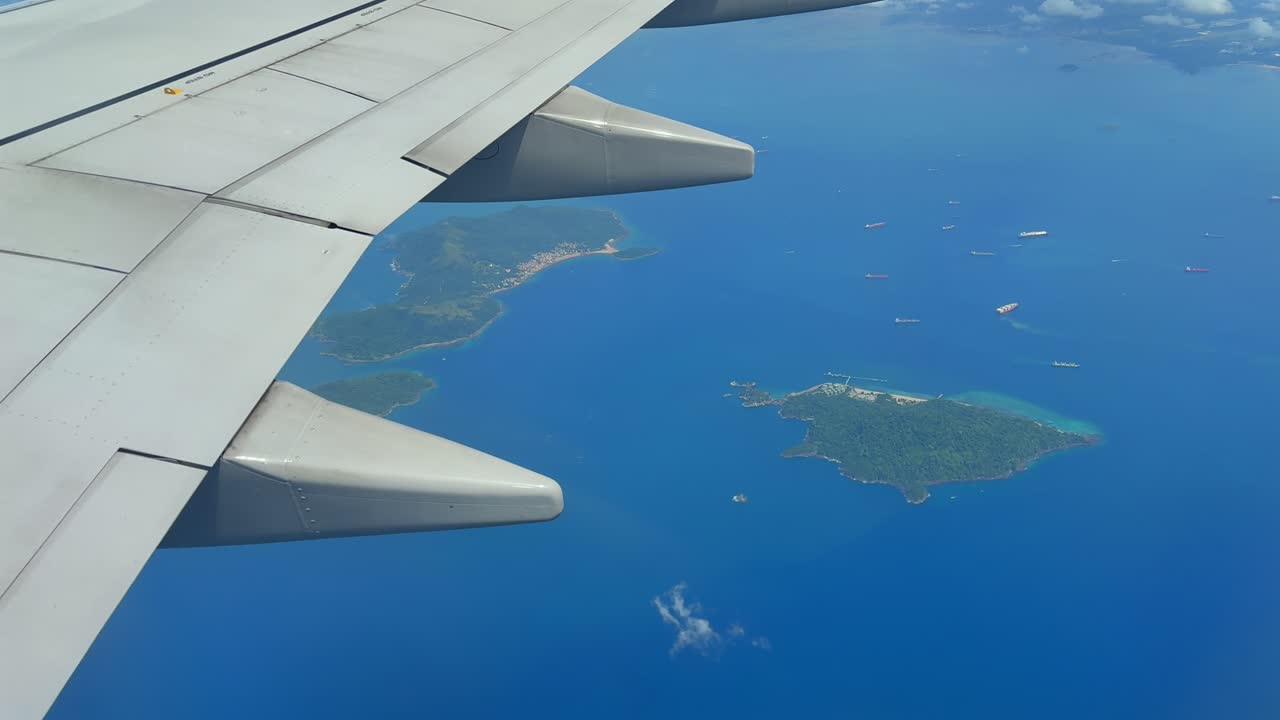 Airplane wing view over tropical blue sea with lush Panama island archipelago and cargo ships below