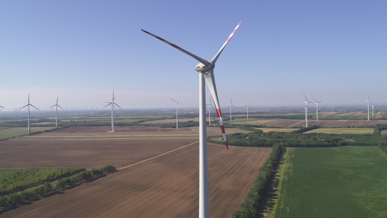 Profile aerial of a static Wind Turbine surrounded by rotating turbines in a flat farmland environment in Monchhof, Austria