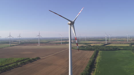 profile aerial of a static wind turbine surrounded by rotating turbines in a flat farmland environment in monchhof, austria