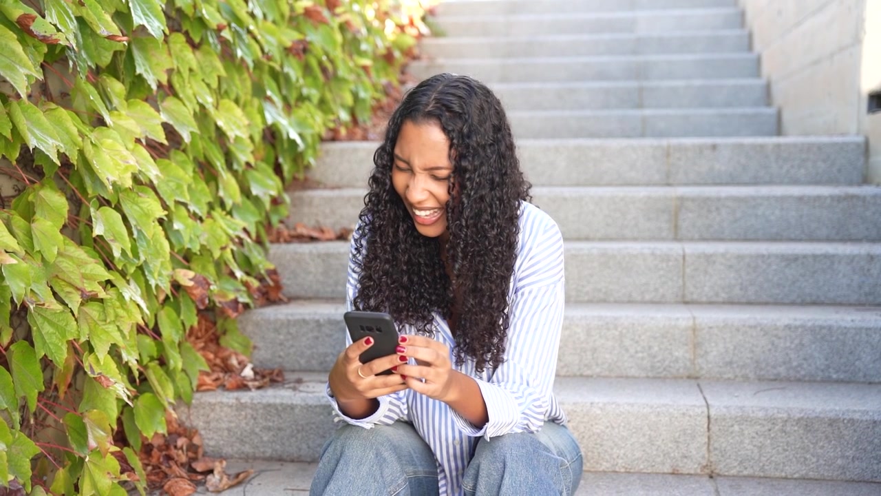 A cheerful young woman is joyfully using her smartphone on the lush green stairs
