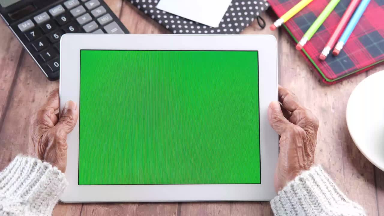 초록색 화면을 가진 태블릿을 사용하는 고령 여성