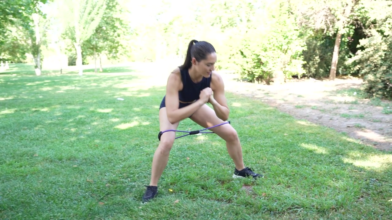 Goditi un allenamento all'aperto con elastici di resistenza con una donna che fa passi laterali in un ambiente naturale.