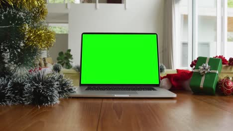 Laptop-with-green-screen-copy-space-on-table-with-santa-hats,-christmas-tree-and-presents