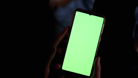 hands female in dark holds and examines smartphone with green touchscreen