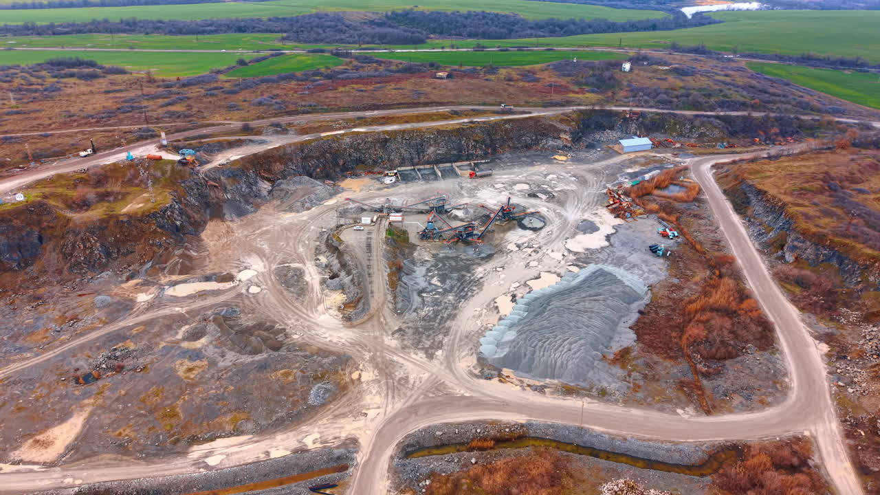 Mining site by a river. A mining area with machines working in the ground. Trucks and equipment are moving around the site
