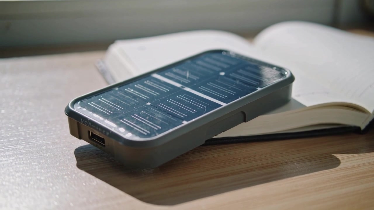 Moving camera revealing grey-cased smartphone on notebook by window, showing USB port reflection