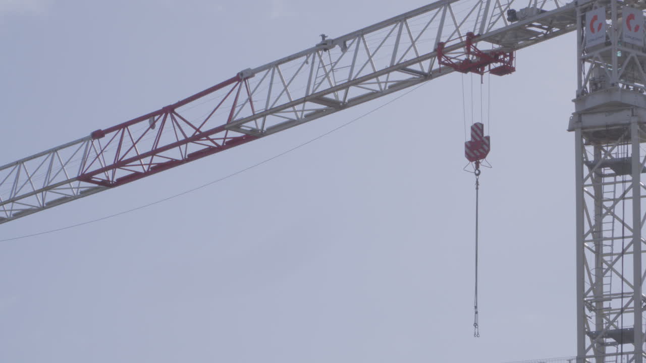 Catena di sollevamento appesa al braccio di una moderna gru a torre eretta contro un cielo nuvoloso. Angolazione bassa, al rallentatore.