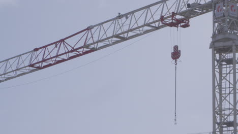 lifting chain hanging from boom of modern tower crane erected against cloudy sky. low angle, slowmo