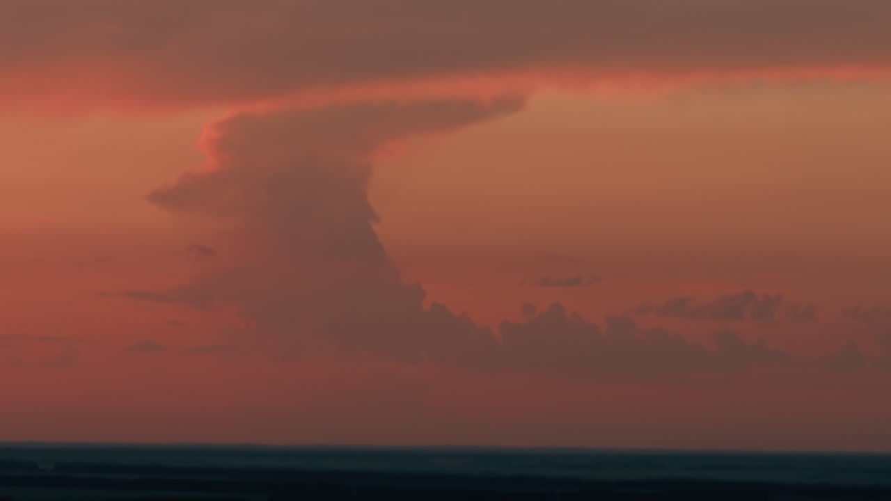 Towering dusk cloud formation illuminated by deep orange sunset glow, vast sky backdrop stretching to distant horizon, serene evening atmosphere