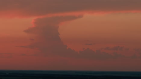 towering dusk cloud formation illuminated by deep orange sunset glow, vast sky backdrop stretching to distant horizon, serene evening atmosphere