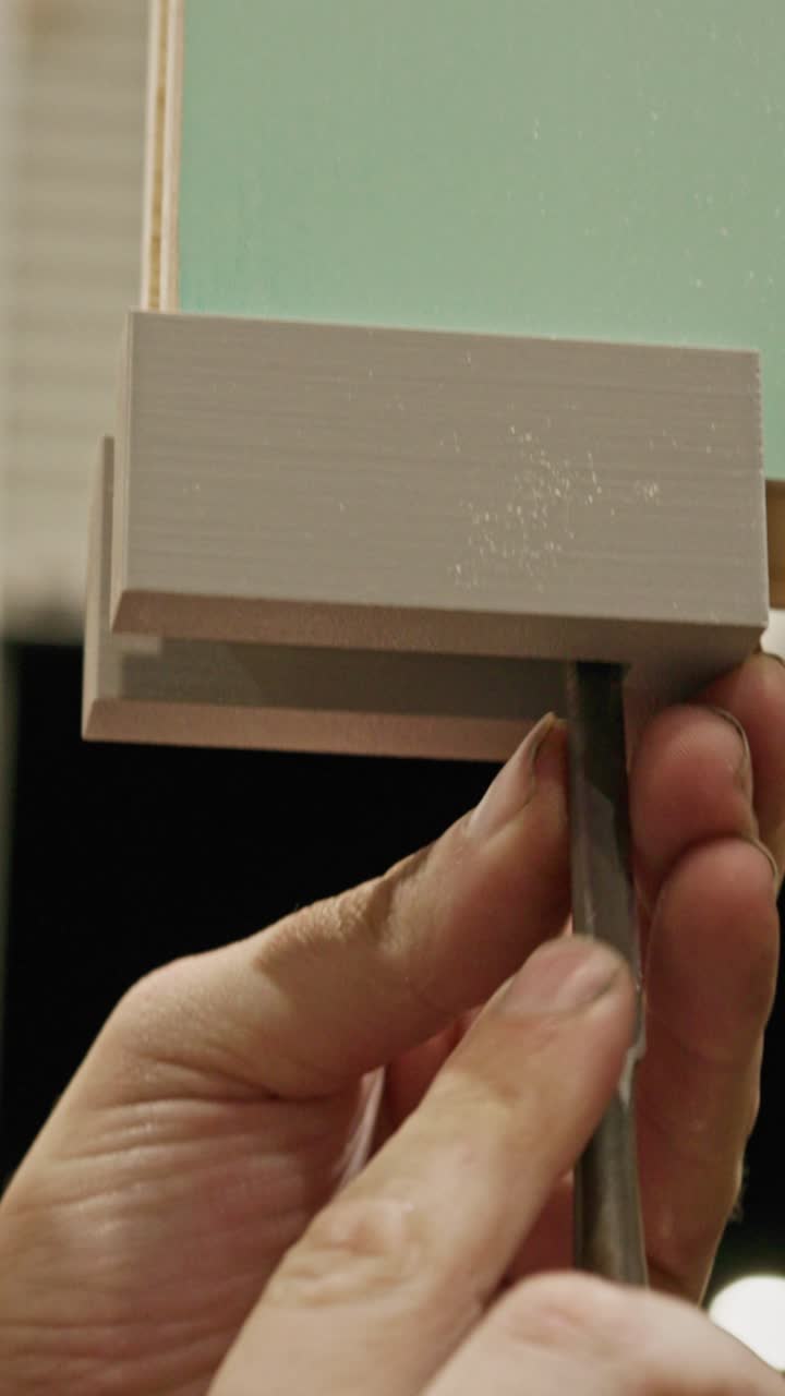 Inquadratura verticale ravvicinata di un artigiano che usa una lima metallica per rimuovere con cura un tappo inferiore della porta (tappo terminale del traverso inferiore) da un componente di porta in legno