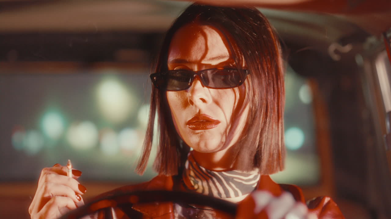 Portrait of Female Driver in Stylish Sunglasses Smoking Inside Car at Night