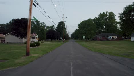 drone shot over street running through neighborhood with homes with garden and trees along with cars on street